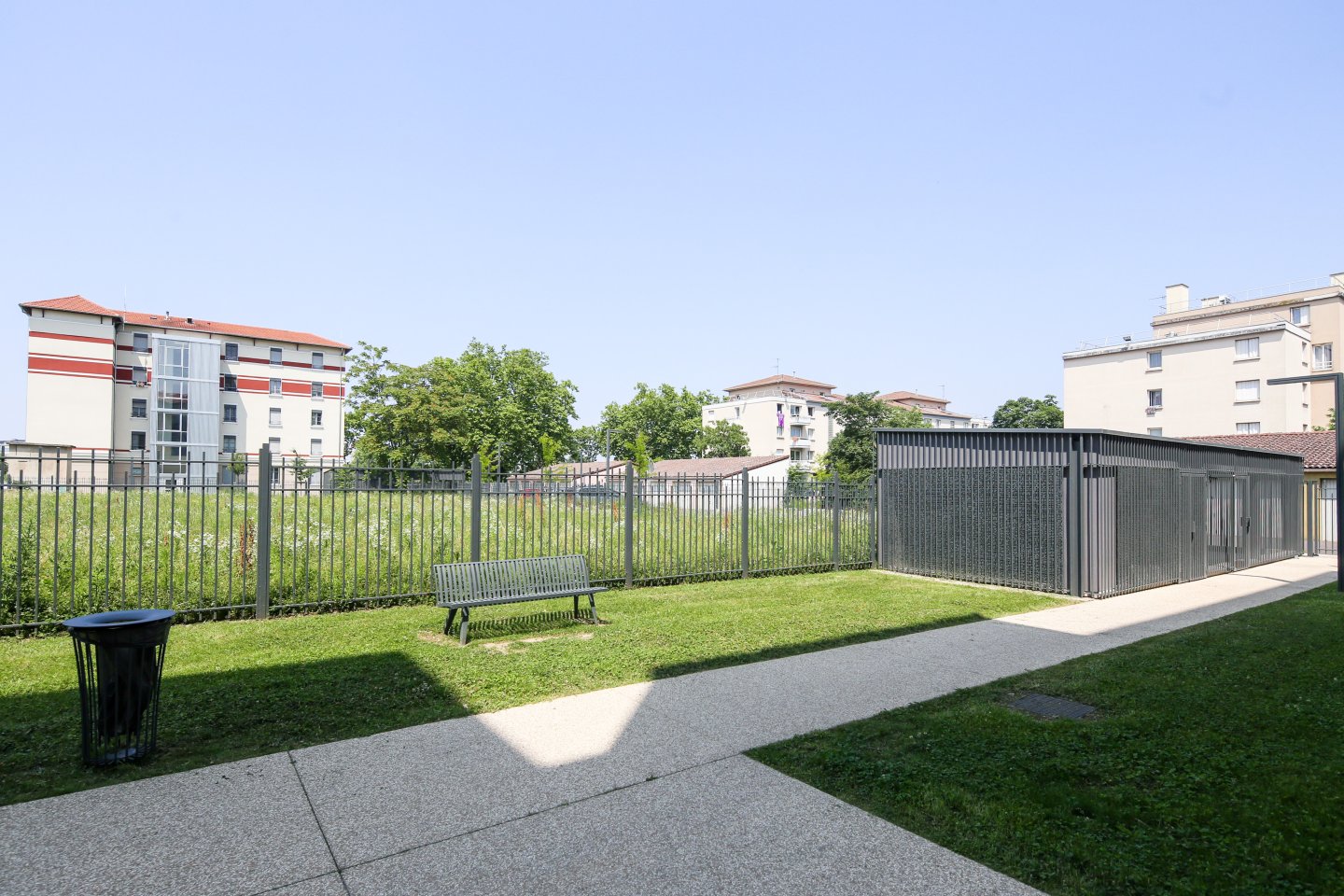 Espace vert avec un local vélo et un banc au pied des Grandes Cités Tase